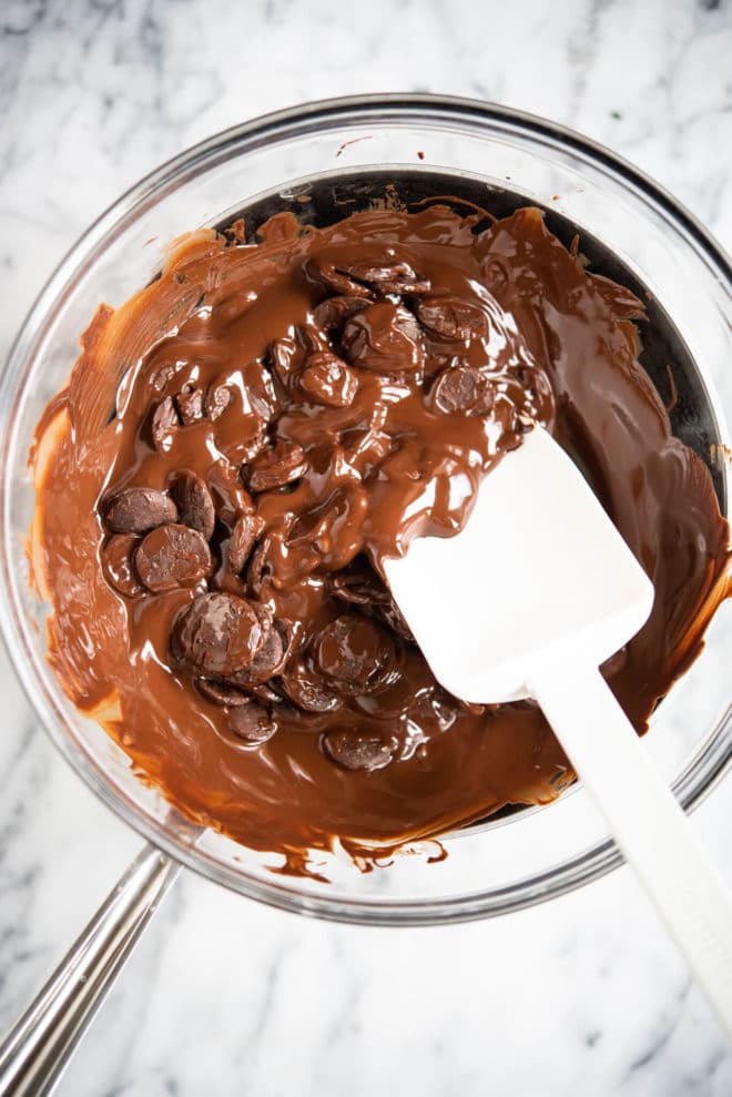 half-melted chocolate in a glass bowl over a stainless steel pot on a marble surface