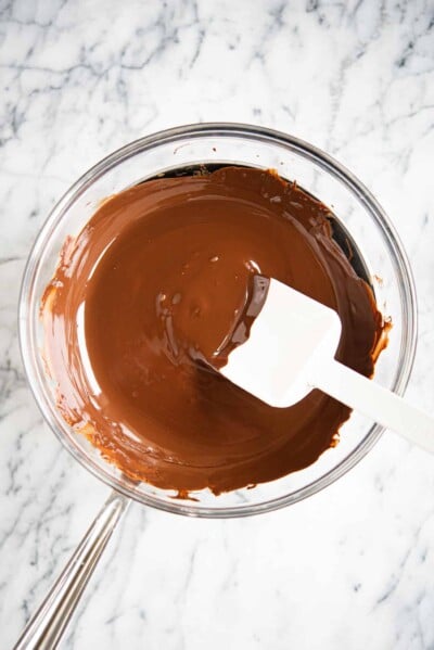 fully melted chocolate in a glass bowl over a stainless steel pot on a marble surface