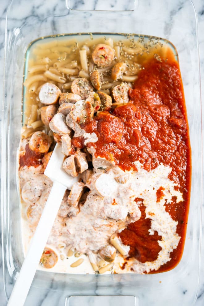 ingredients for easy pasta bake being mixed together in a glass baking dish on a marble surface