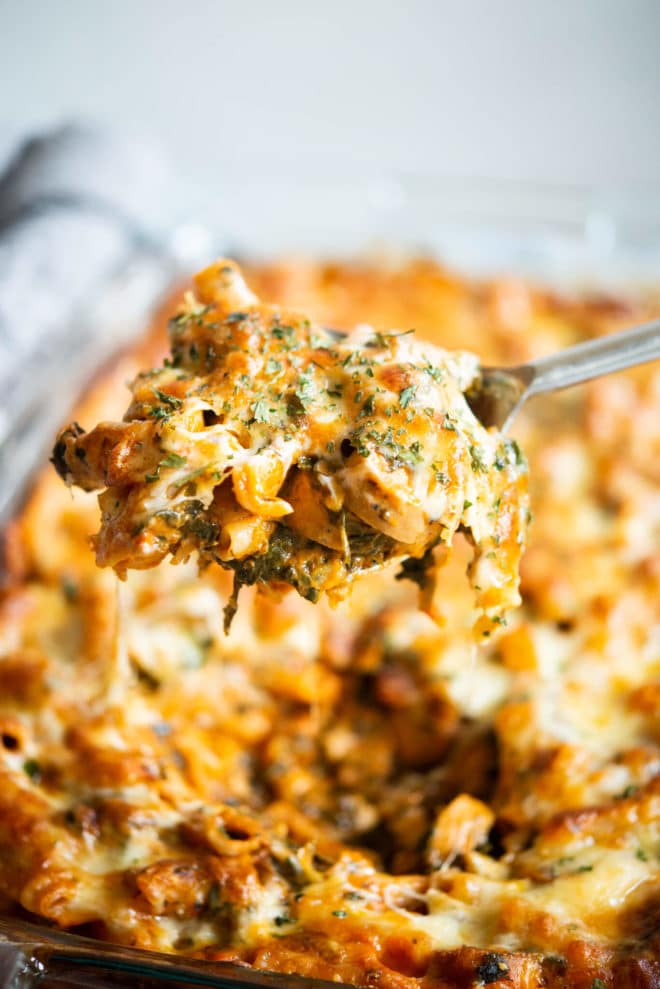 spoonful of cheesy no boil pasta bake hovering over a glass baking dish filled with cheesy pasta