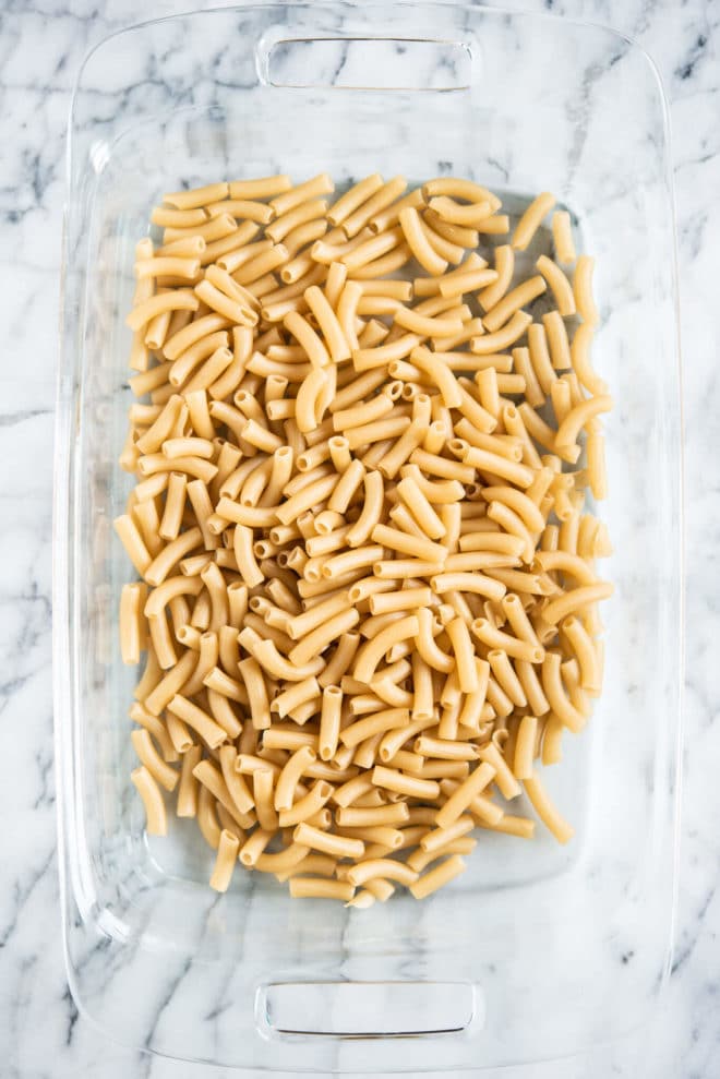uncooked penne pasta in a glass baking dish on a marble surface