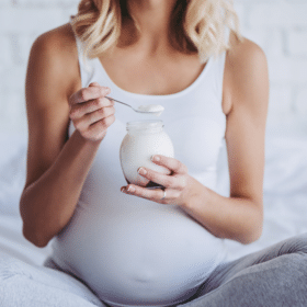 pregnant woman sitting in bed eating yogurt - what to eat in your second trimester