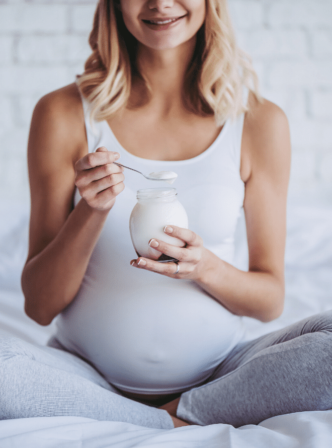 pregnant woman sitting in bed eating yogurt - what to eat in your second trimester