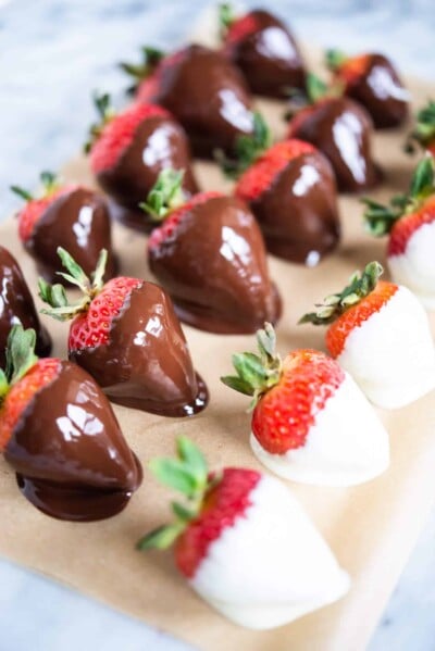 strawberries dipped in white and dark chocolate on parchment paper on a marble surface