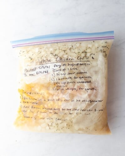 white chicken chili ingredients including broth, chicken, and corn frozen in a clear zip top bag with writing on it