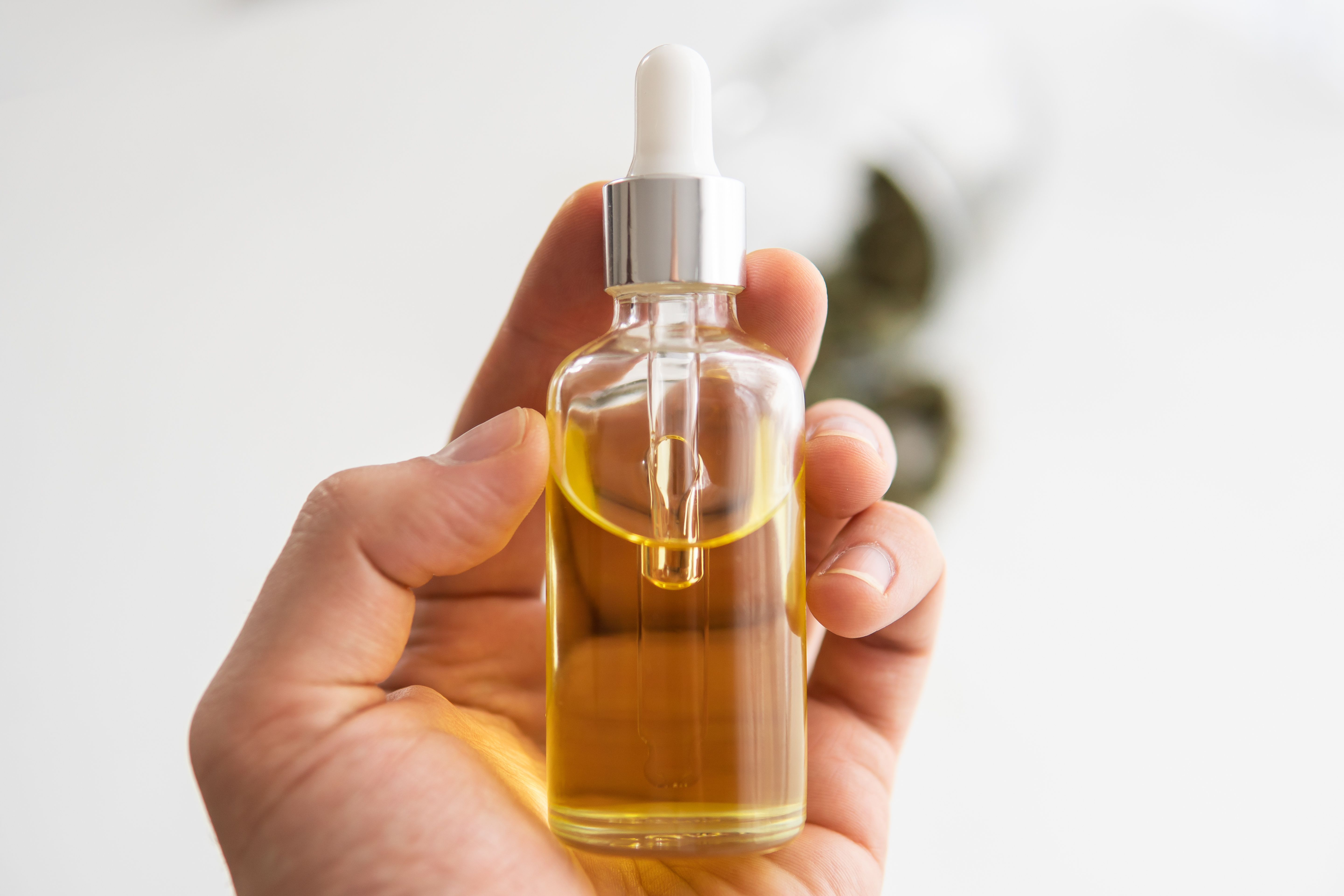 a person's hand holding a clear dropper bottle of CBD oil