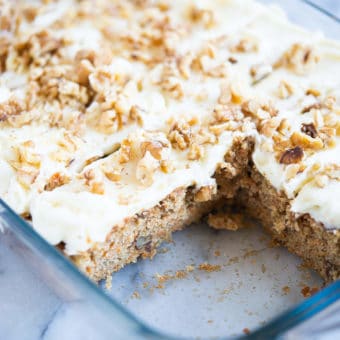 iced carrot cake cut into pieces with two pieces missing in a clear baking dish on a marble surface