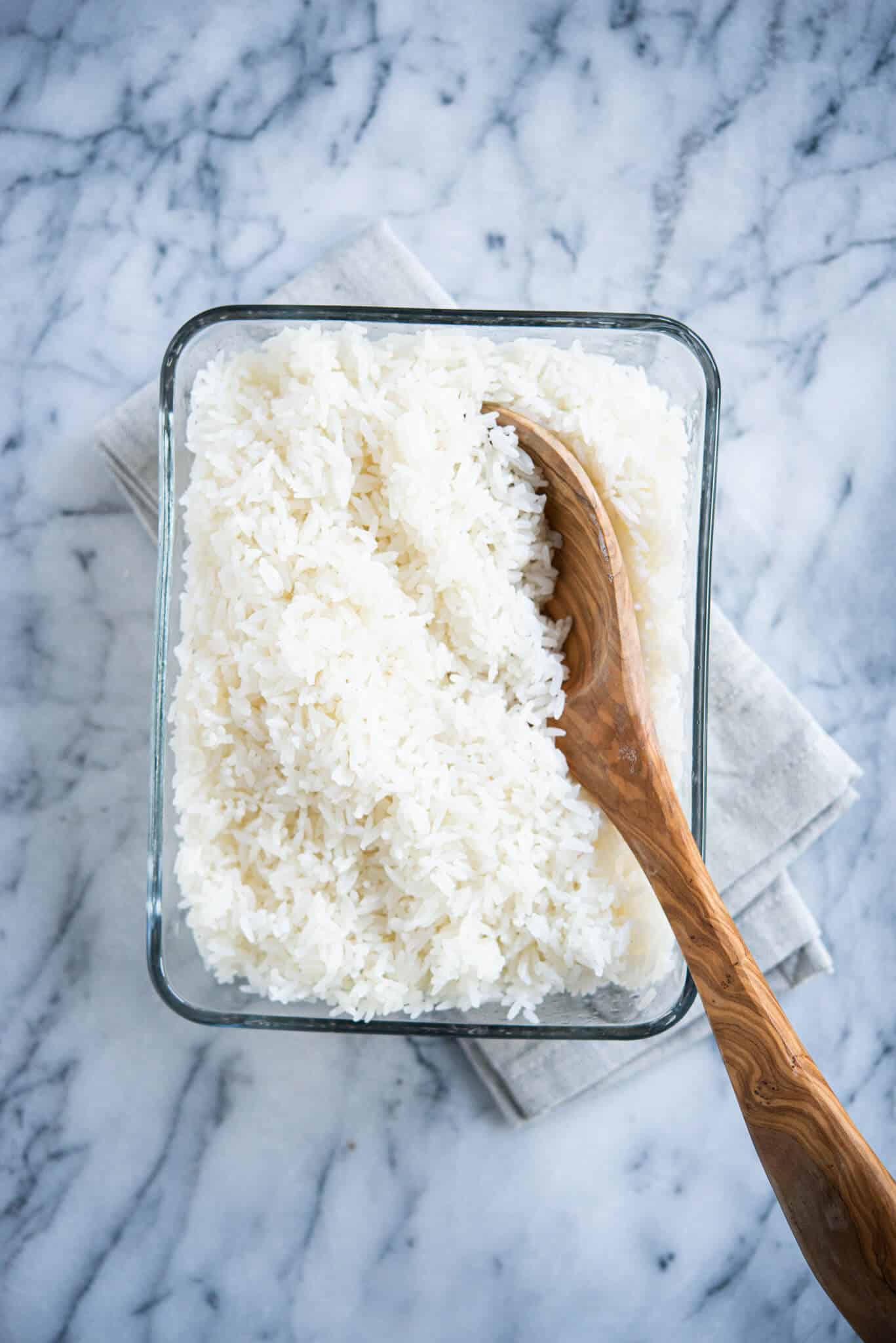 cooked white coconut rice in a glass dish with a wooden spoon on a marble surface