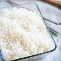 cooked white coconut rice in a glass dish with a wooden spoon on a marble surface