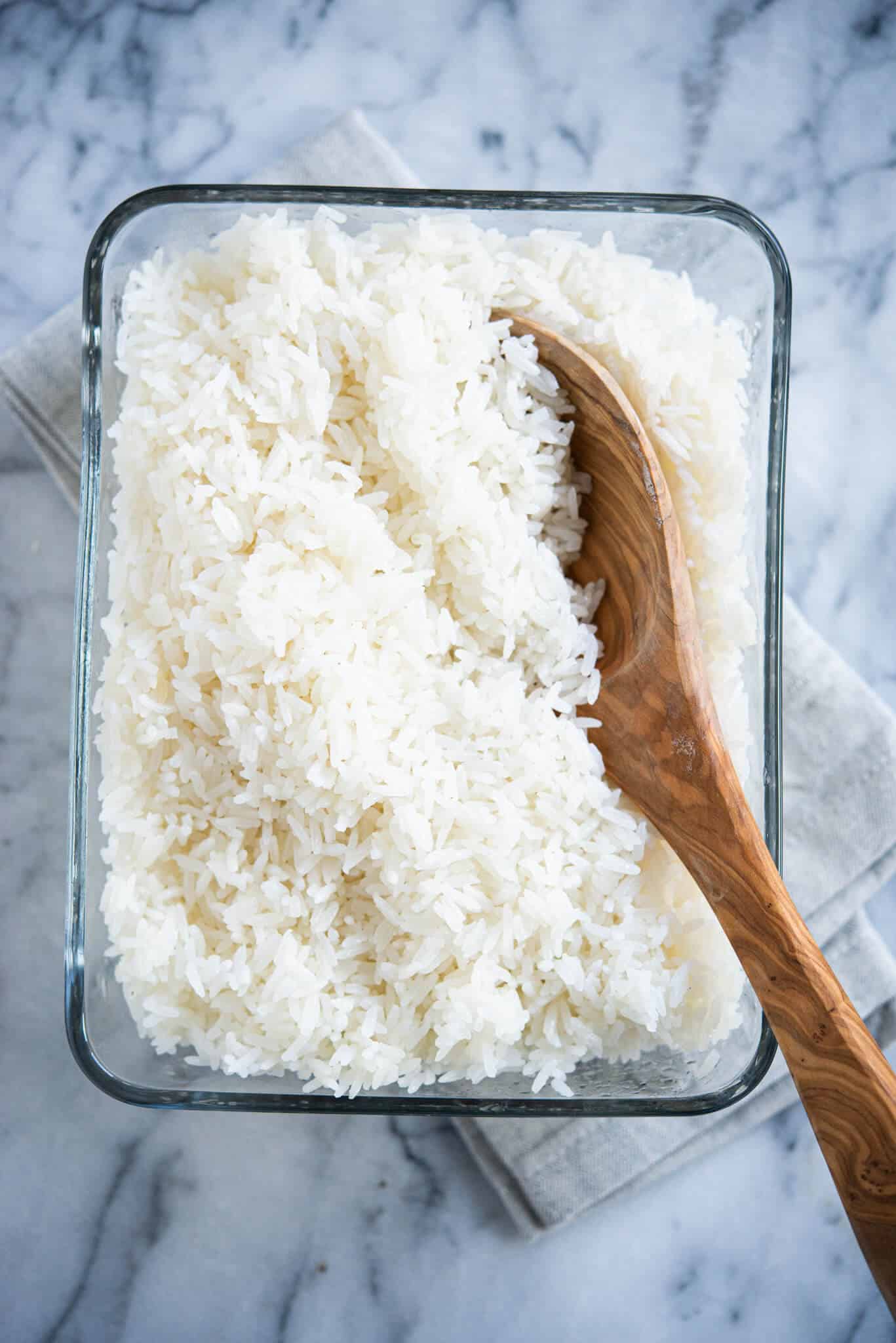 cooked white coconut rice in a glass dish with a wooden spoon on a marble surface