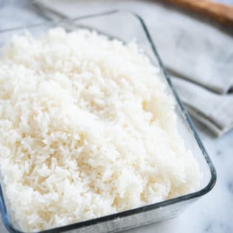 cooked white coconut rice in a glass dish with a wooden spoon on a marble surface