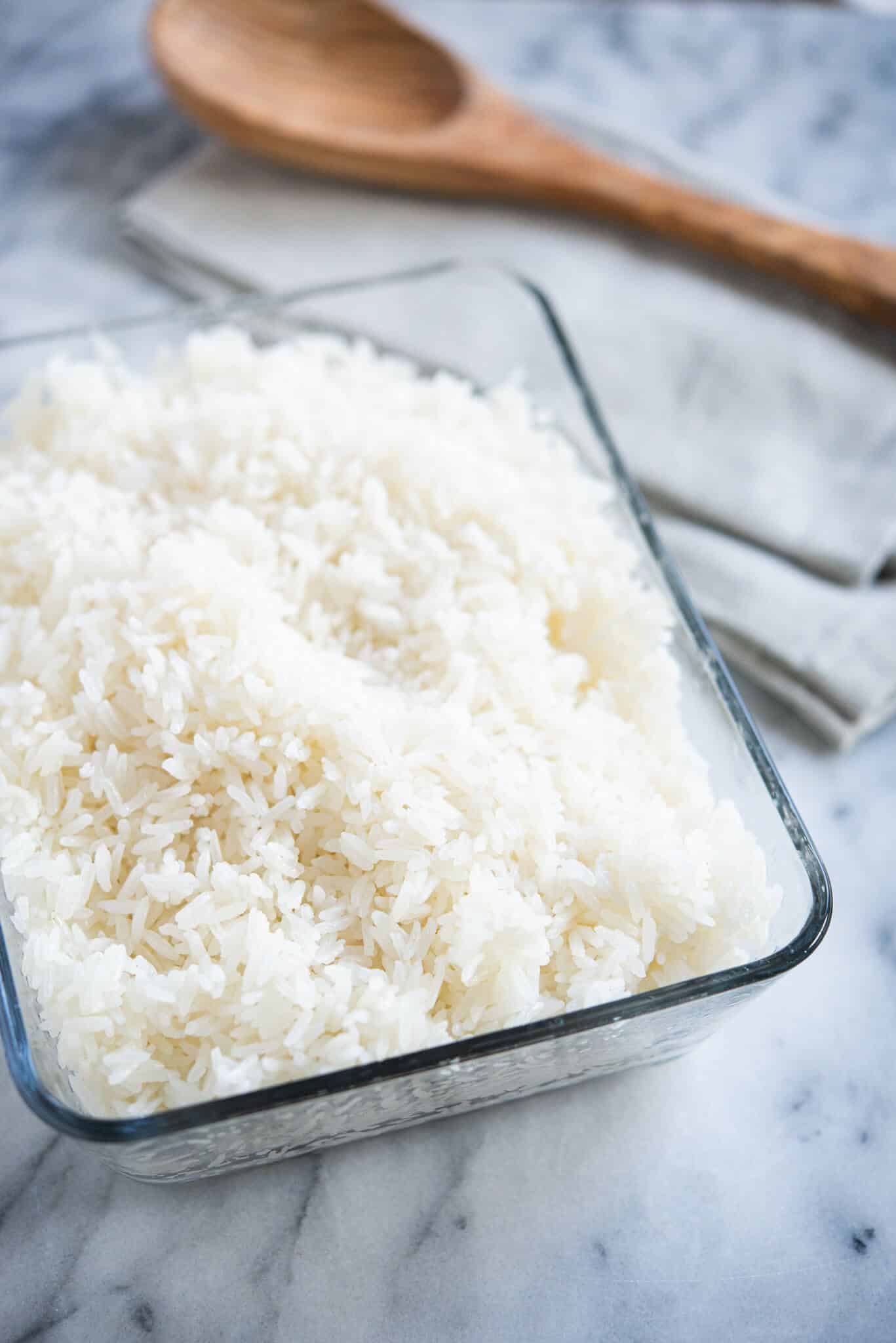 cooked white coconut rice in a glass dish with a wooden spoon on a marble surface