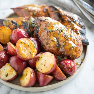 Seared honey mustard chicken and halved red potatoes on a grey plate on a marble surface