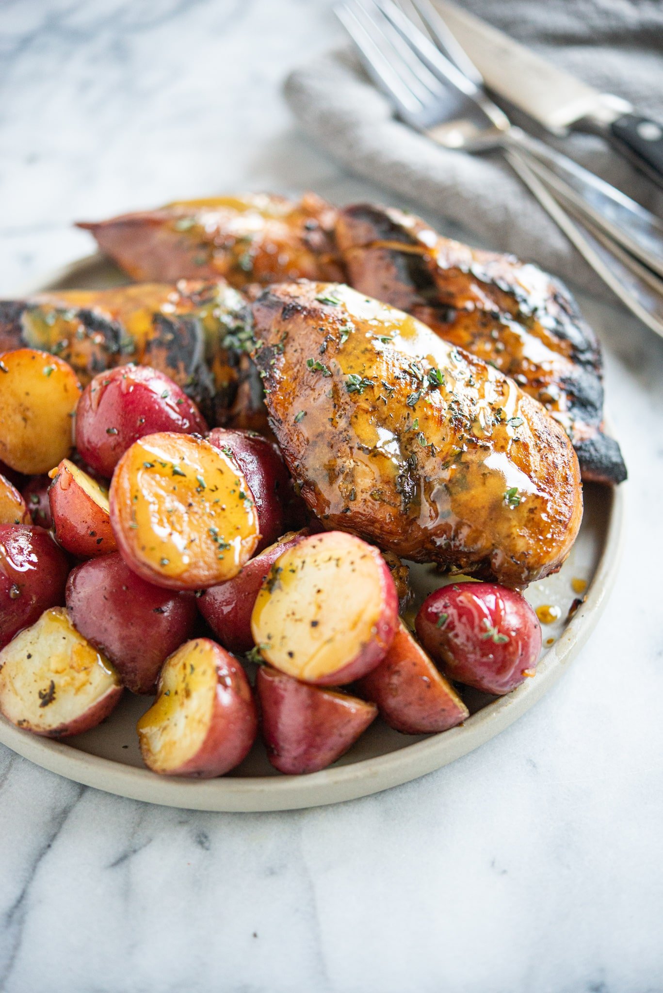 Seared honey mustard chicken and halved red potatoes on a grey plate on a marble surface