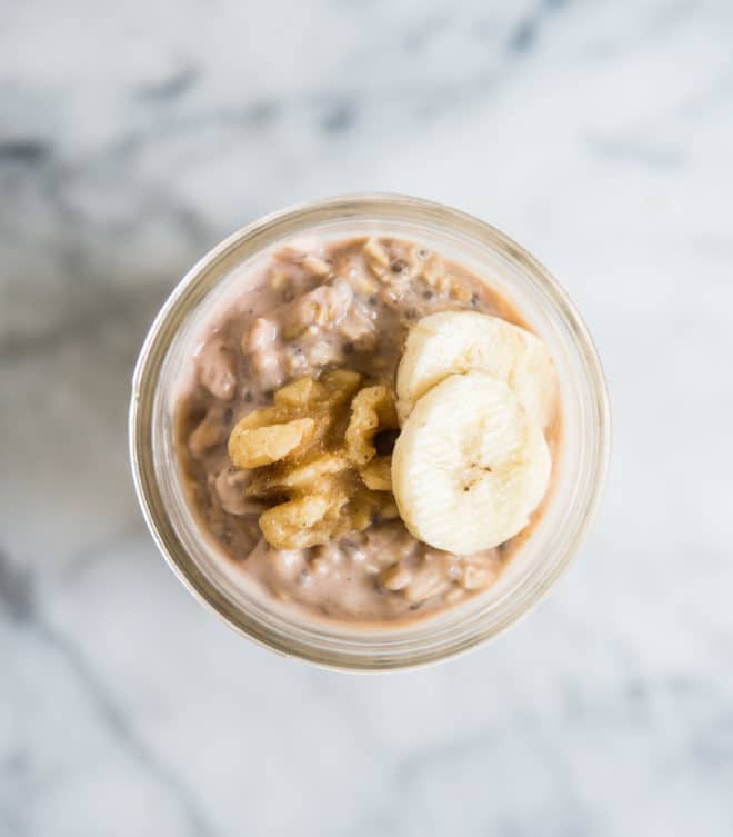 banana nut overnight oats with sliced bananas and walnuts on top in a glass mason jar on a marble surface