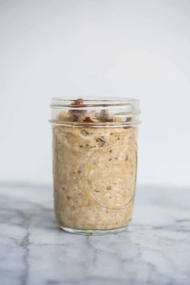 pumpkin overnight oats in a glass mason jar with pecans and cinnamon on top on a marble surface