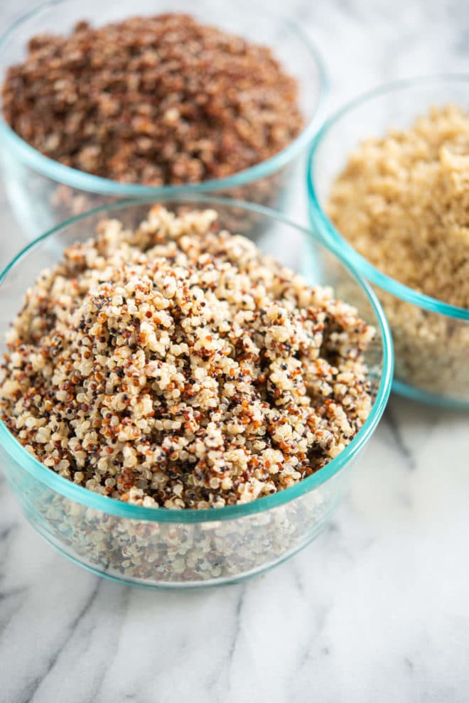 perfectly cooked tri-color, red, and white quinoa in circular glass bowls on a marble surface