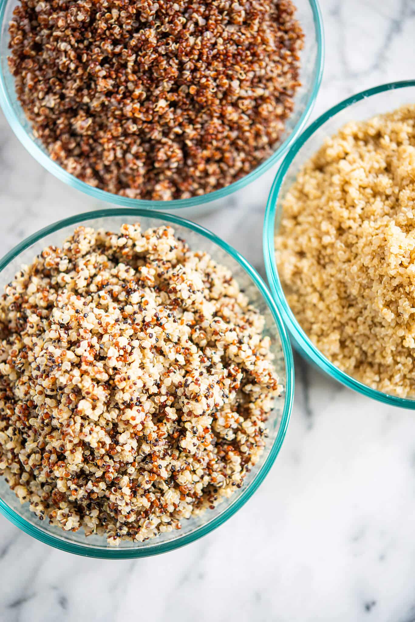 perfectly cooked tri-color, red, and white quinoa in circular glass bowls on a marble surface