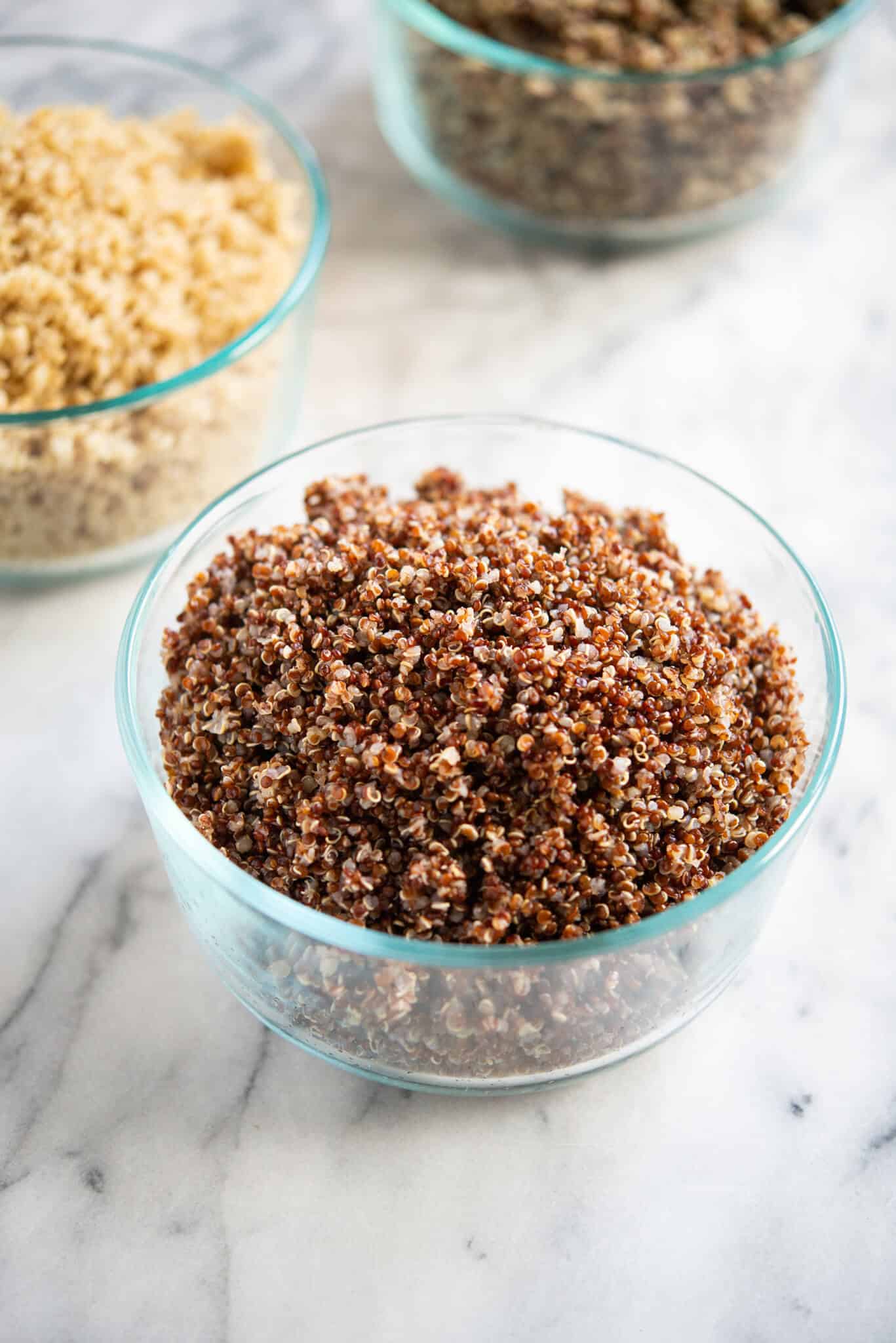 perfectly cooked tri-color, red, and white quinoa in circular glass bowls on a marble surface