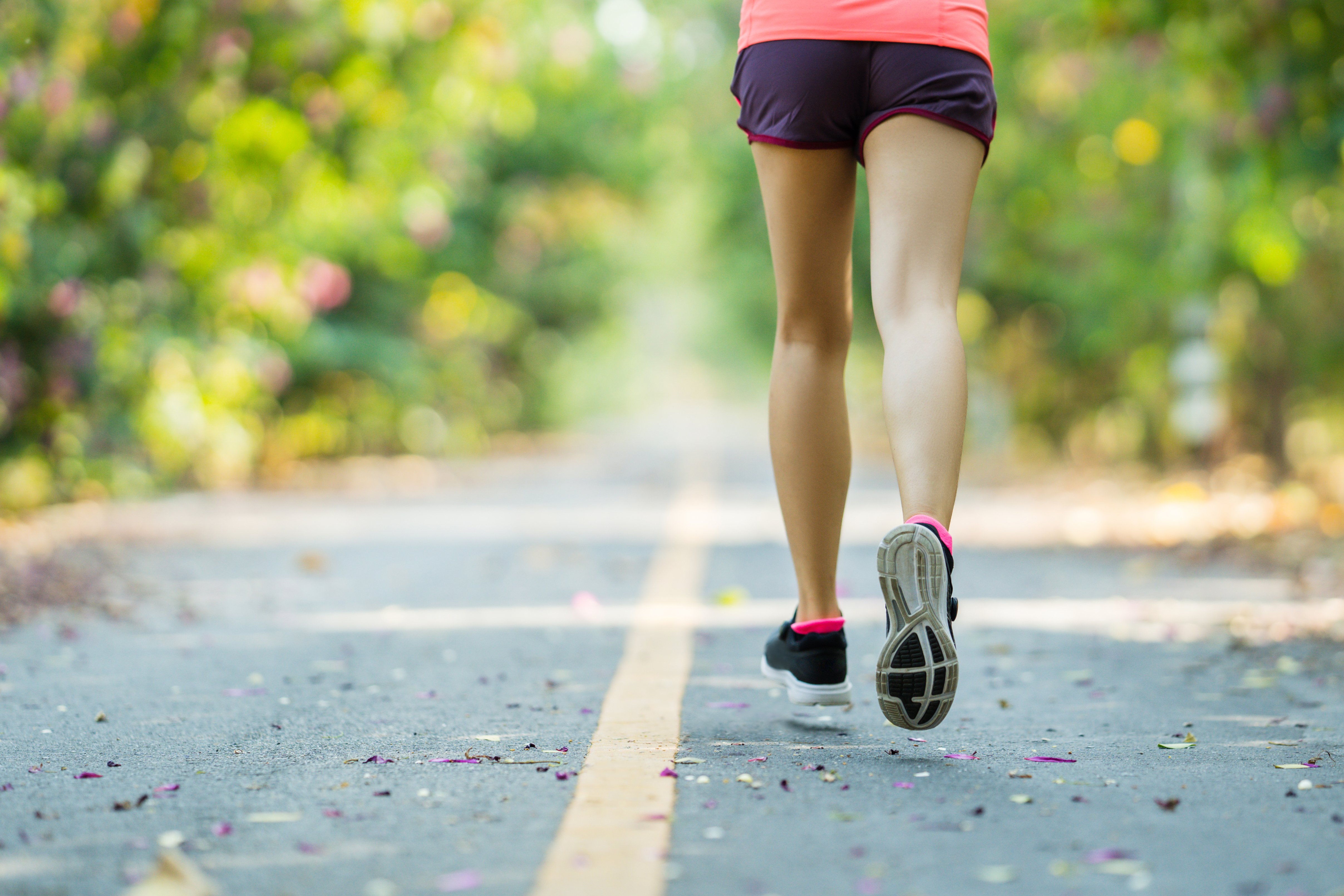 bottom half of woman running on a greenery filled trail
