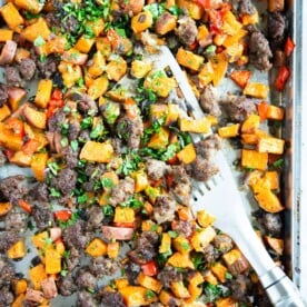 crumbled sausage, bell pepper, and sweet potato breakfast hash on a sheet pan with a silver spatula on it on a marble surface
