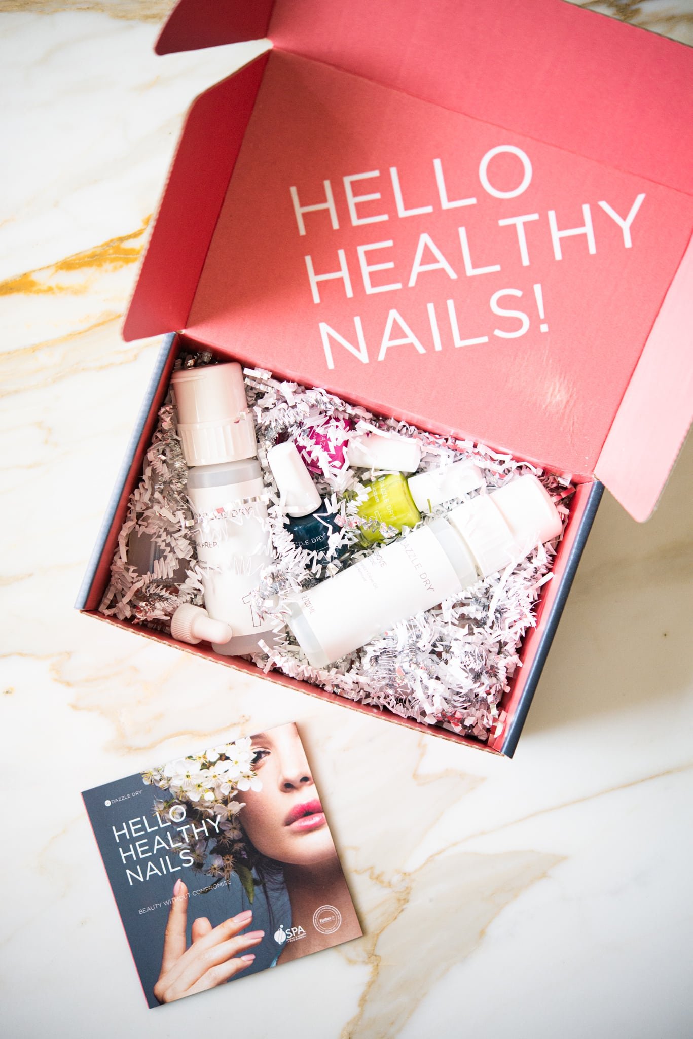 pink box filled with 3 colors of nail polish, two clear polishes, and polish remover on a marble surface