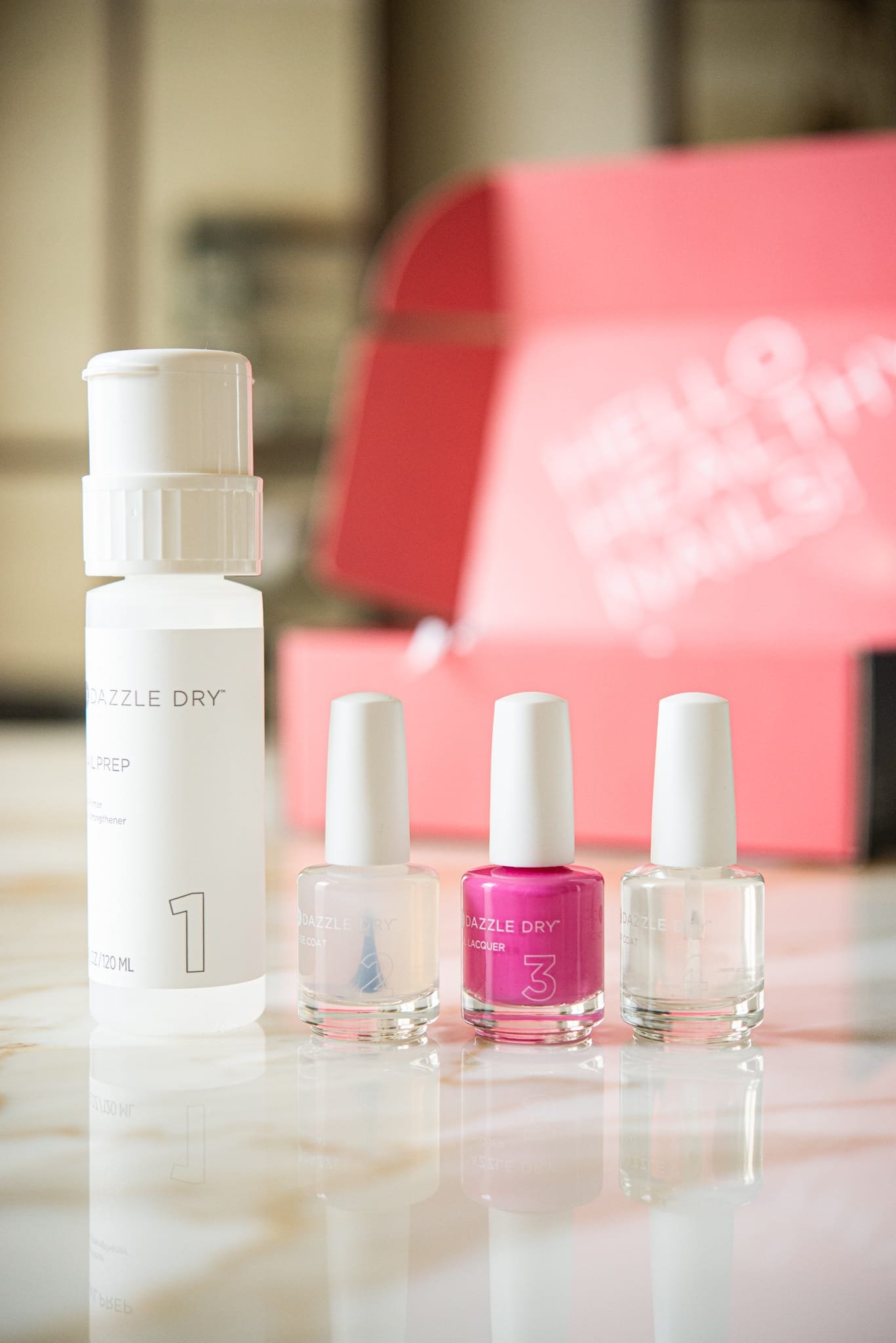 dazzle dry nail system - bright pink nail polish next to two clear nail polishes and a remover, on a marble table