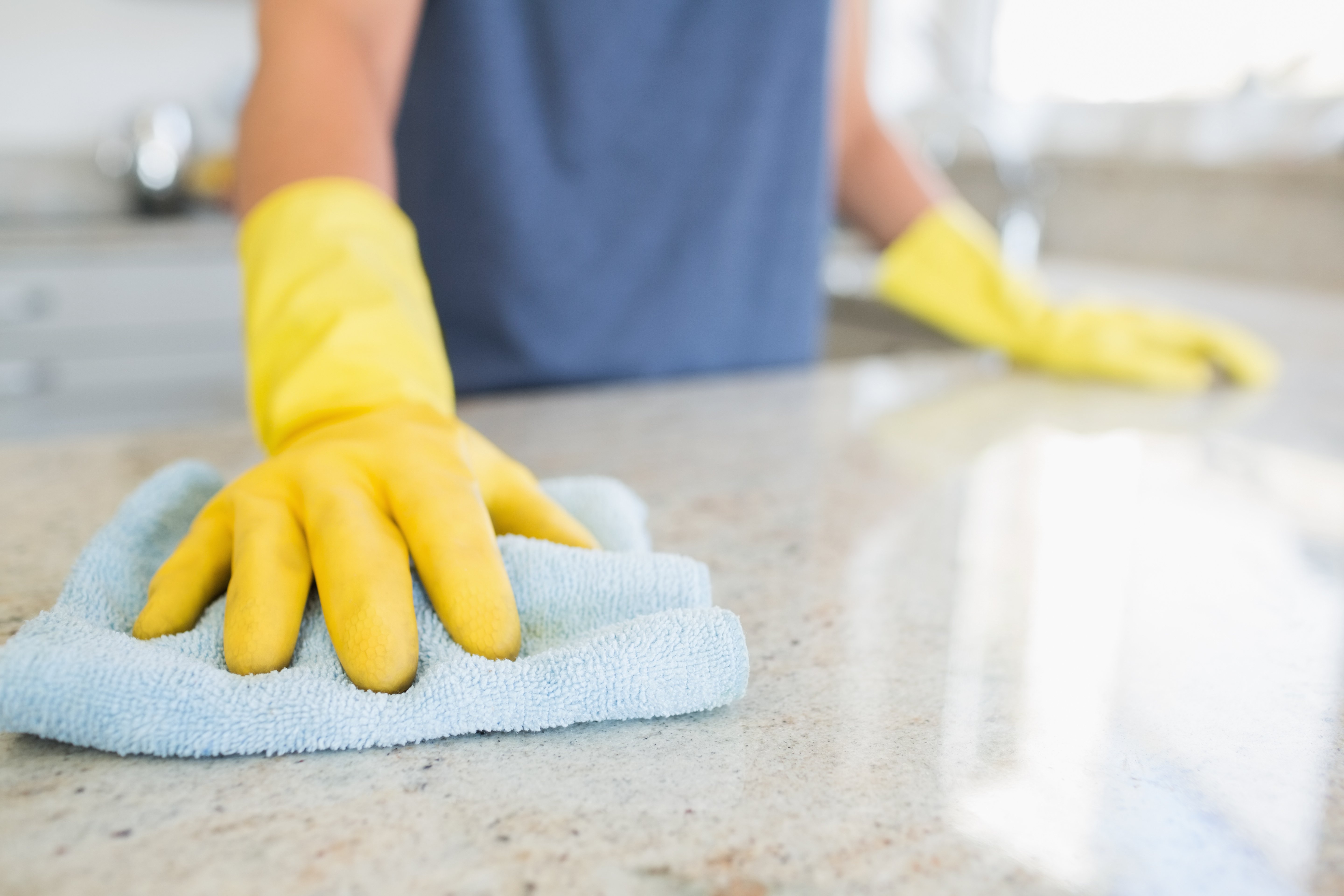 woman wearing yellow cleaning gloves wiping kitchen counter with blue towel