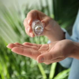 Woman using antibacterial hand gel with greenery in background, closeup