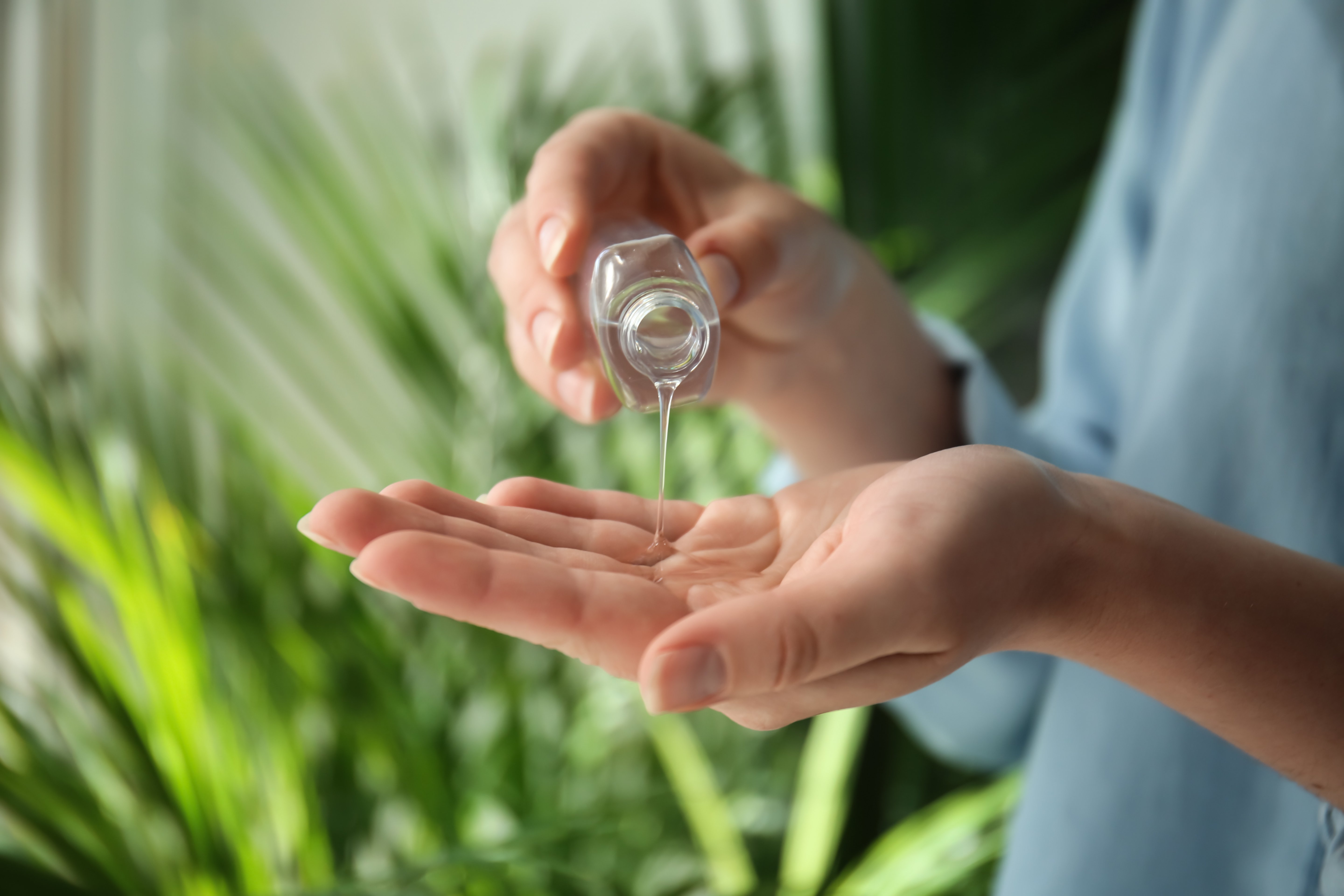 Woman using antibacterial hand gel with greenery in background, closeup