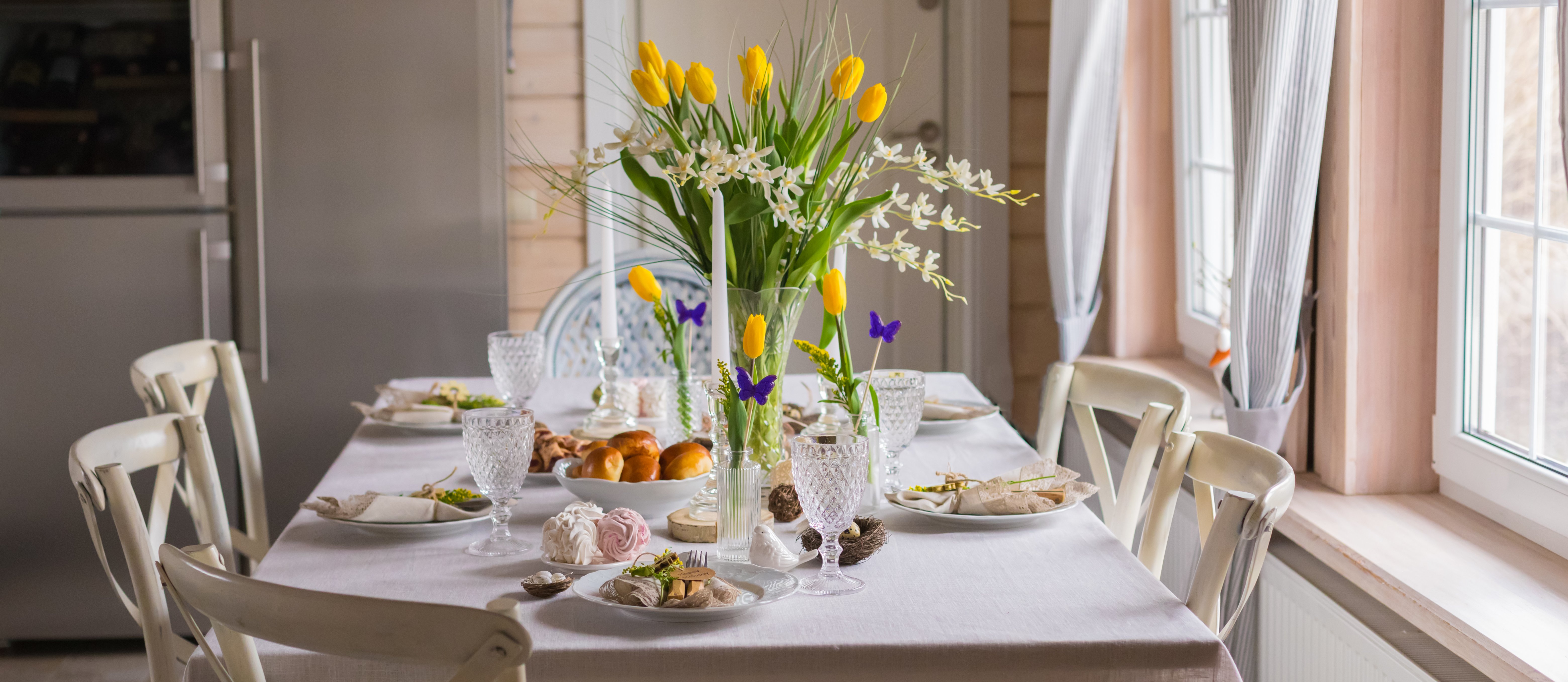 Easter festive spring table setting decoration, eggs in nest, fresh yellow tulips in vase, marshmallows, feathers, family dinner or breakfast concept, toned