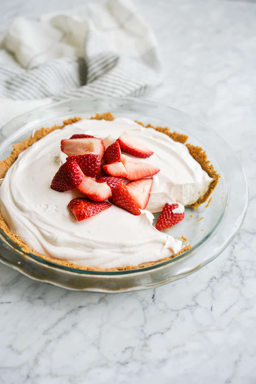 strawberry yogurt pie with a slice taken out of it topped with quartered strawberries on a marble surface