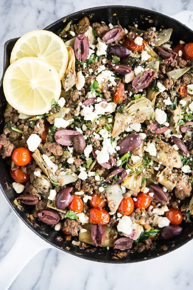 mediterranean skillet with spinach, feta, olives, and artichokes in a cast iron pan on a marble surface