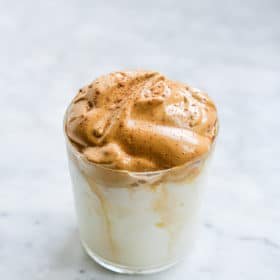 dalgona coffee - glass of iced milk topped with frothy whipped coffee on a marble surface