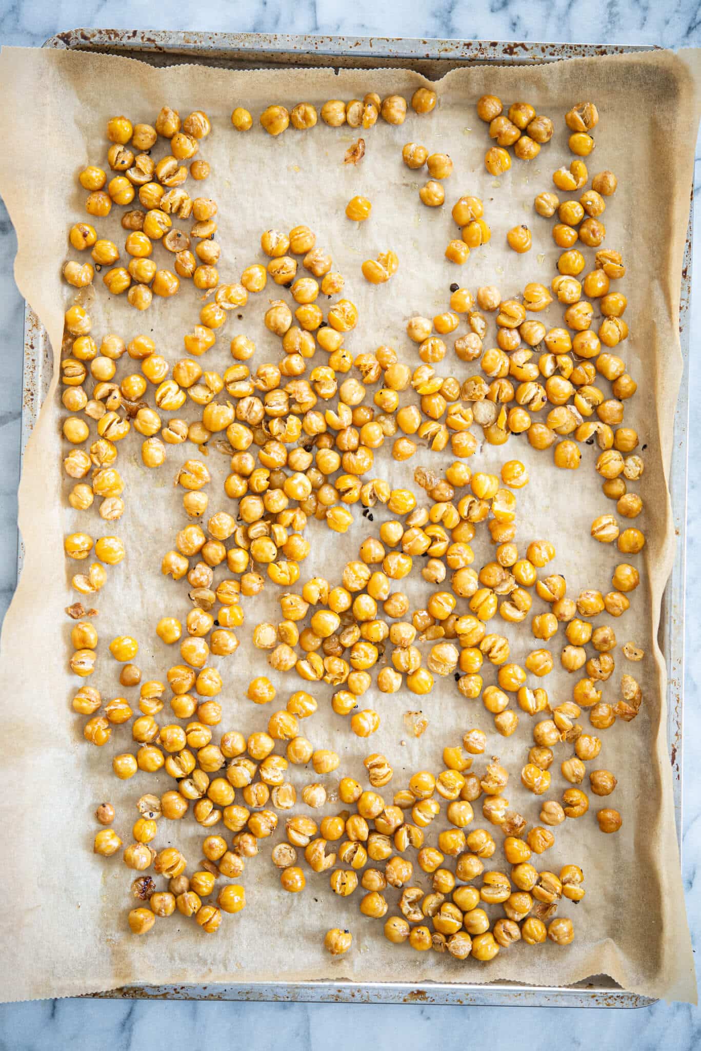 crispy roasted chickpeas on a parchment paper lined baking sheet on a marble surface