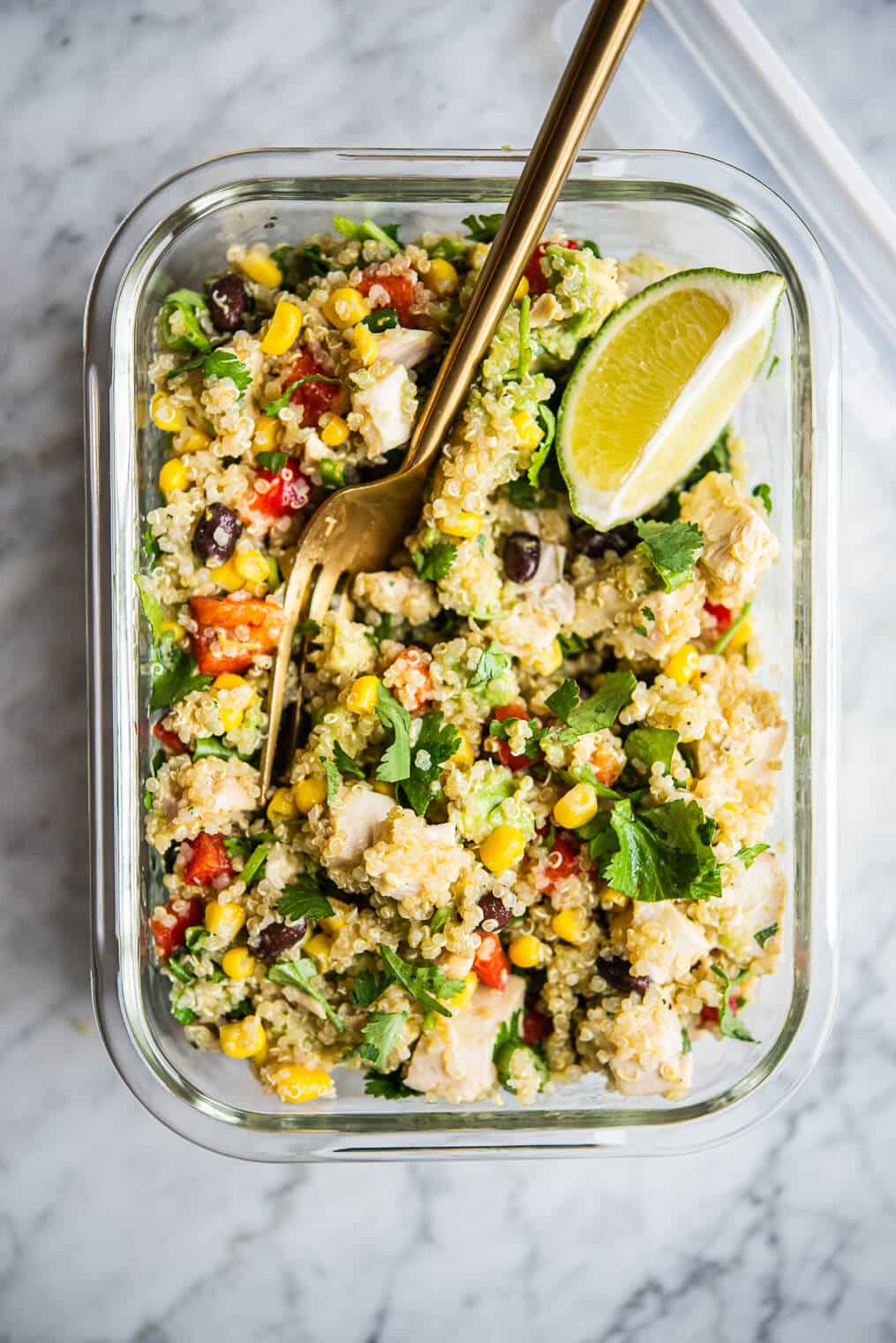 southwestern quinoa salad garnished with a lime wedge and cilantro in a glass bowl on a marble surface