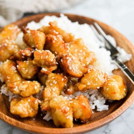 general tso's chicken and white rice in a wooden bowl with a fork on a marble surface