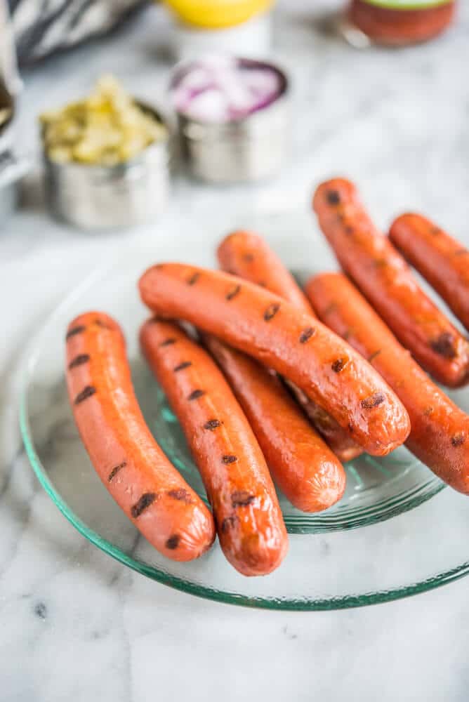 hot dogs, buns, mustard, ketchup, cheese, relish, and onions ready for a hot dog bar on a marble surface