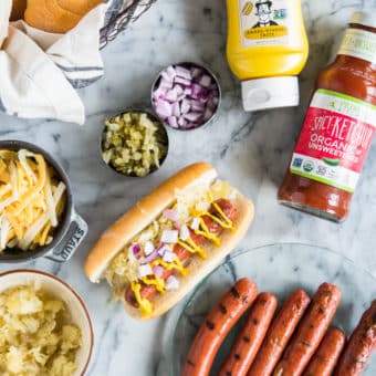 hot dogs, buns, mustard, ketchup, cheese, relish, and onions ready for a hot dog bar on a marble surface