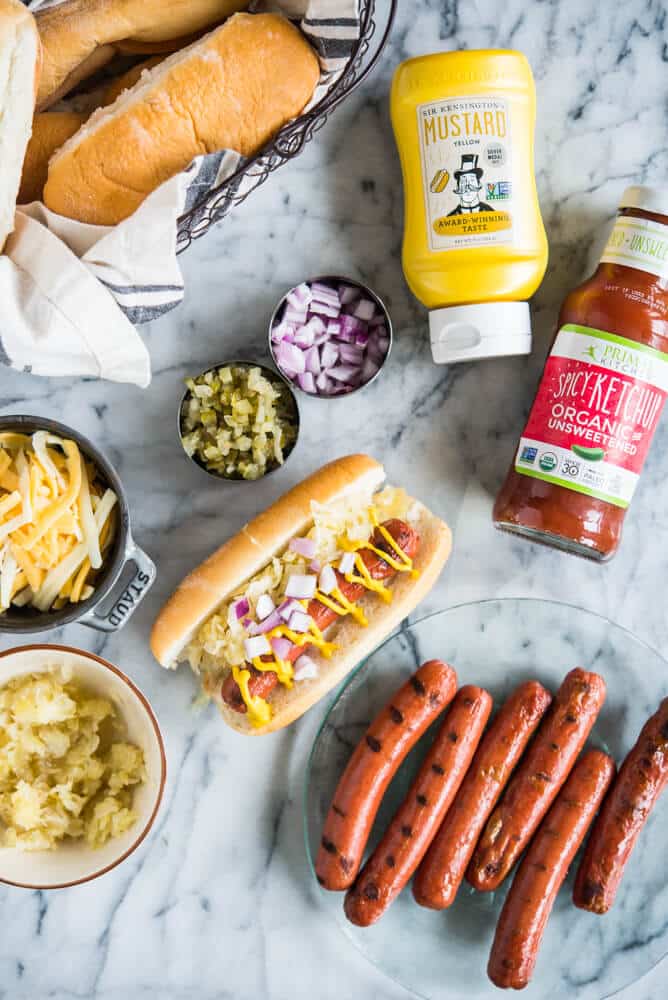 hot dogs, buns, mustard, ketchup, cheese, relish, and onions ready for a hot dog bar on a marble surface