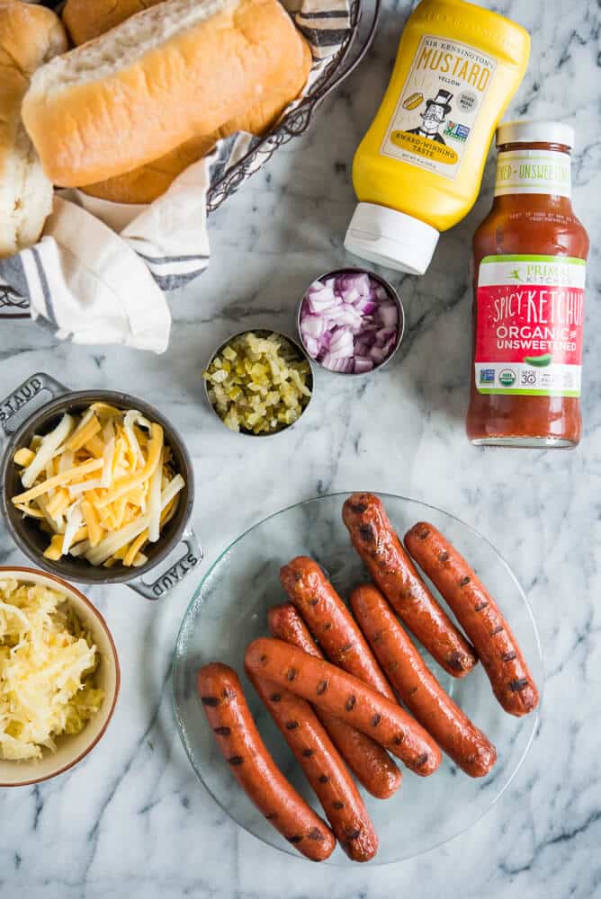 hot dogs, buns, mustard, ketchup, cheese, relish, and onions ready for a hot dog bar on a marble surface