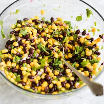 corn and black bean salsa in a large glass bowl with a metal spoon on a marble surface