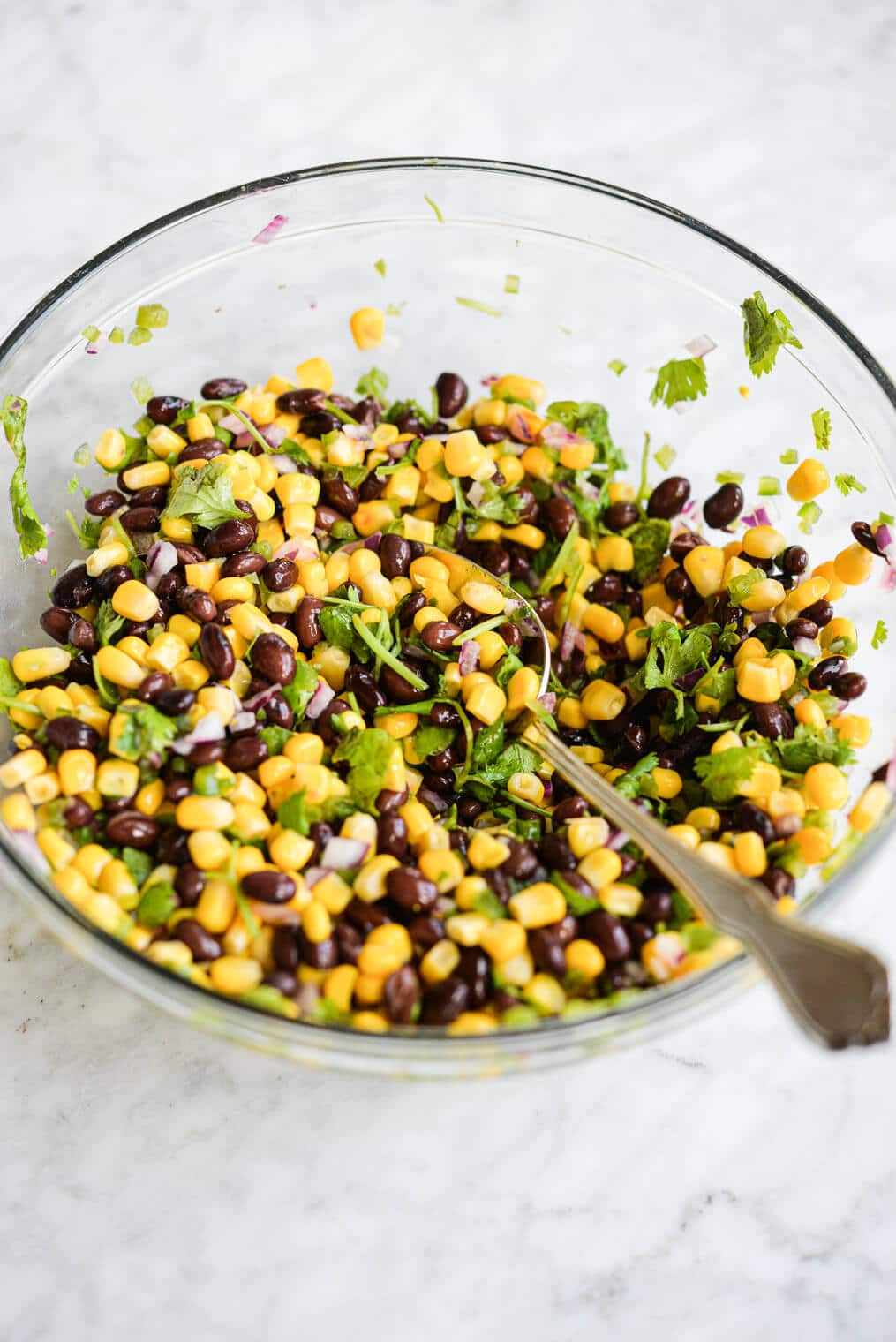 corn and black bean salsa in a large glass bowl with a metal spoon on a marble surface