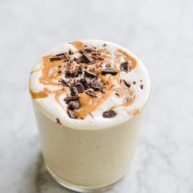 a peanut butter banana smoothie topped with peanut butter and chocolate in a glass cup on a marble surface