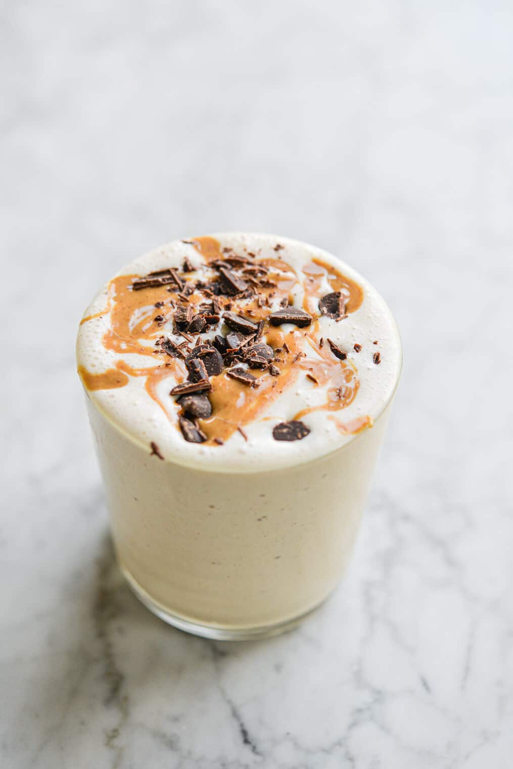 a peanut butter banana smoothie topped with peanut butter and chocolate in a glass cup on a marble surface