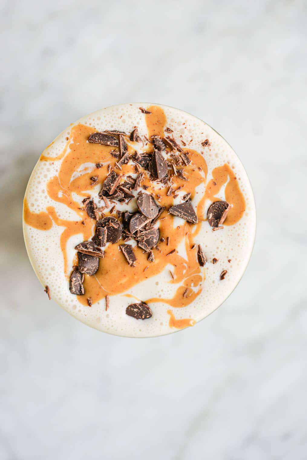 a peanut butter banana smoothie topped with peanut butter and chocolate in a glass cup on a marble surface