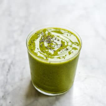 a tropical green smoothie topped with chia seeds on a marble surface