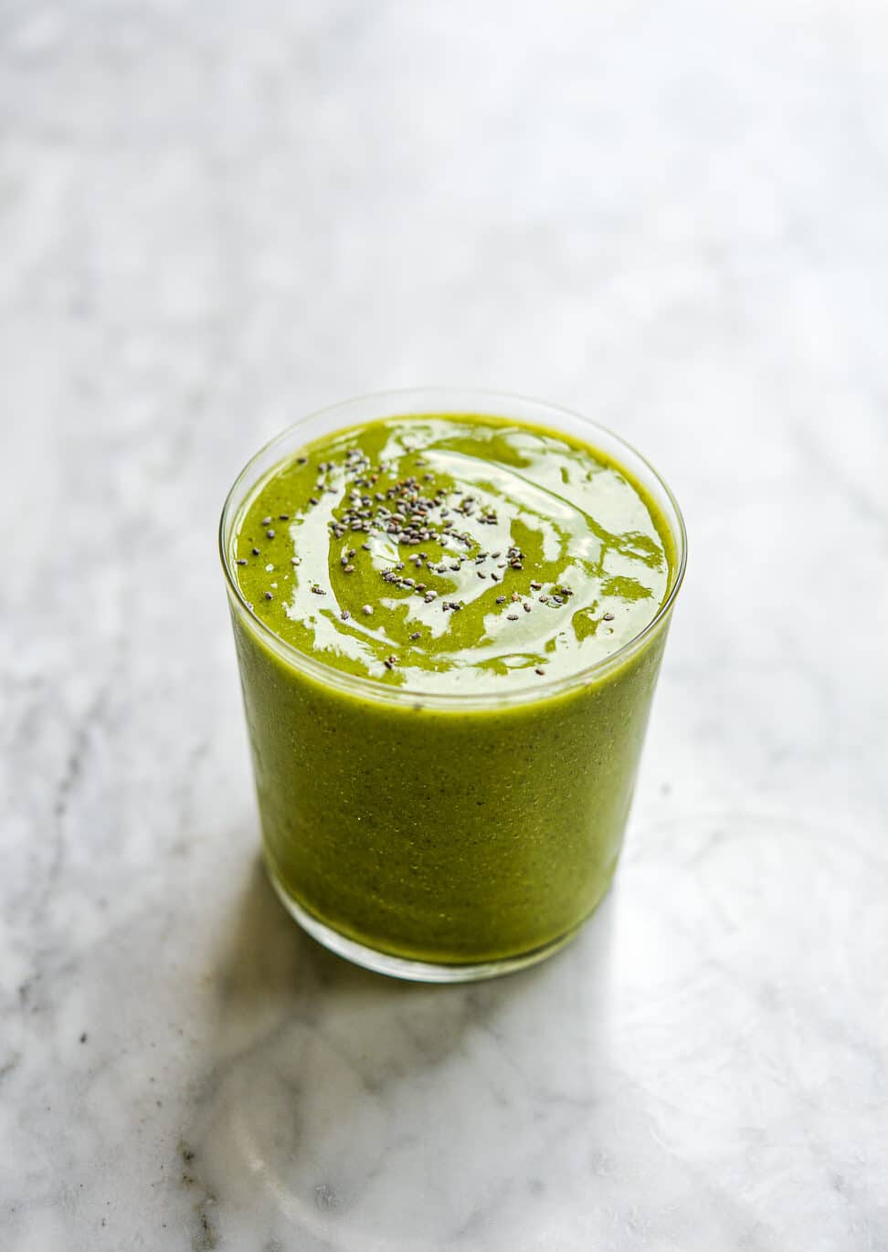 a tropical green smoothie topped with chia seeds on a marble surface