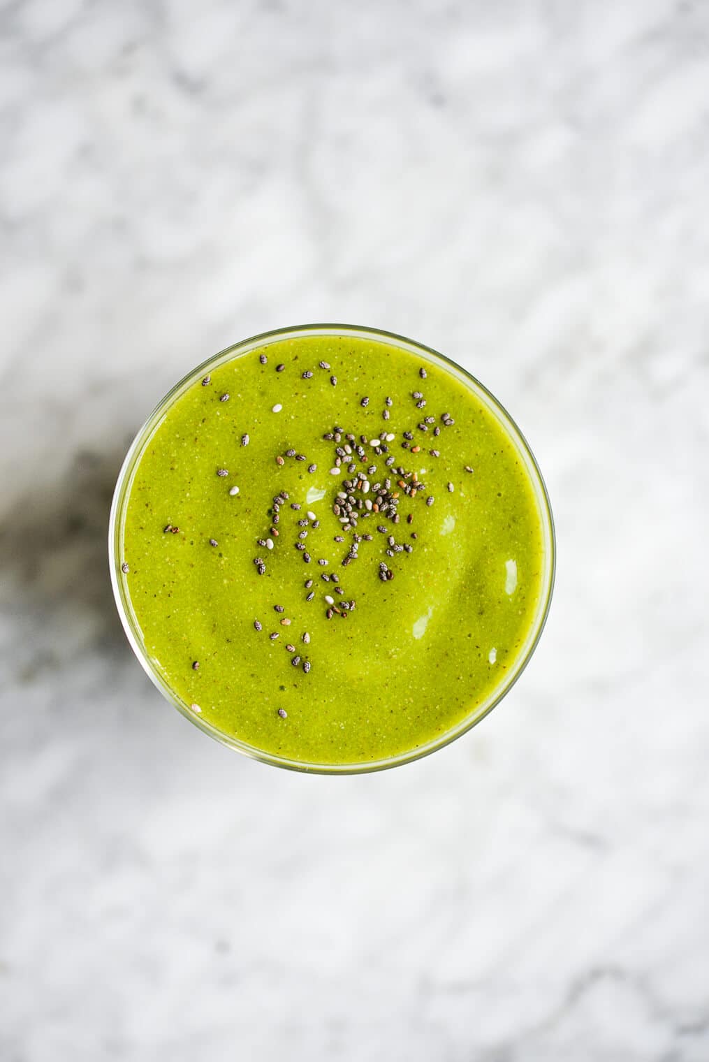 top view of a tropical green smoothie topped with chia seeds on a marble surface