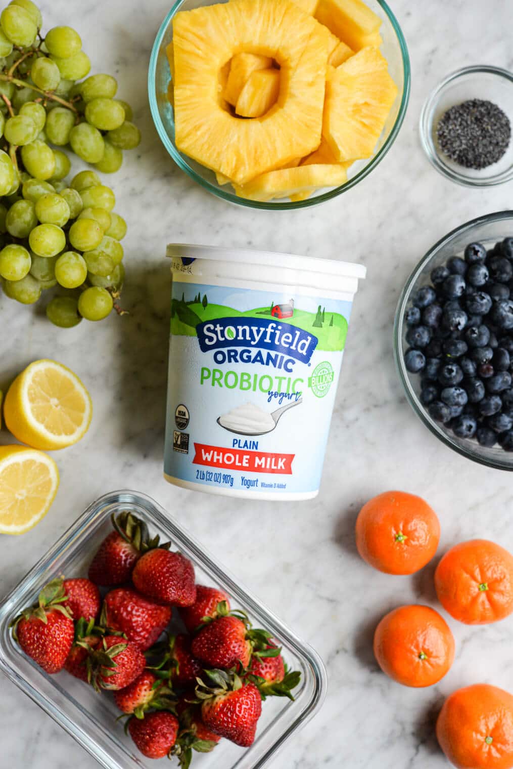 a container of stonyfield organic yogurt, next to fruit for a yogurt fruit salad on a marble surface